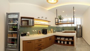Eine moderne Küche mit integriertem Kühlschrank, Mikrowelle und Kaffeemaschine. Ein Regal zeigt Einmachgläser und einen kleinen Topf mit Pflanze.