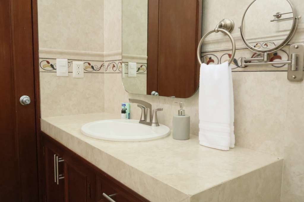 A bathroom with a sink, mirror, towel rack, and a bottle of hand soap.