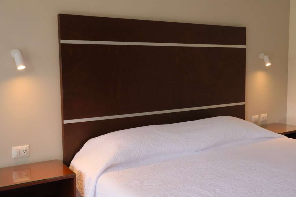 Une chambre d’hôtel avec un grand lit, une tête de lit sombre et deux lampes de chevet.