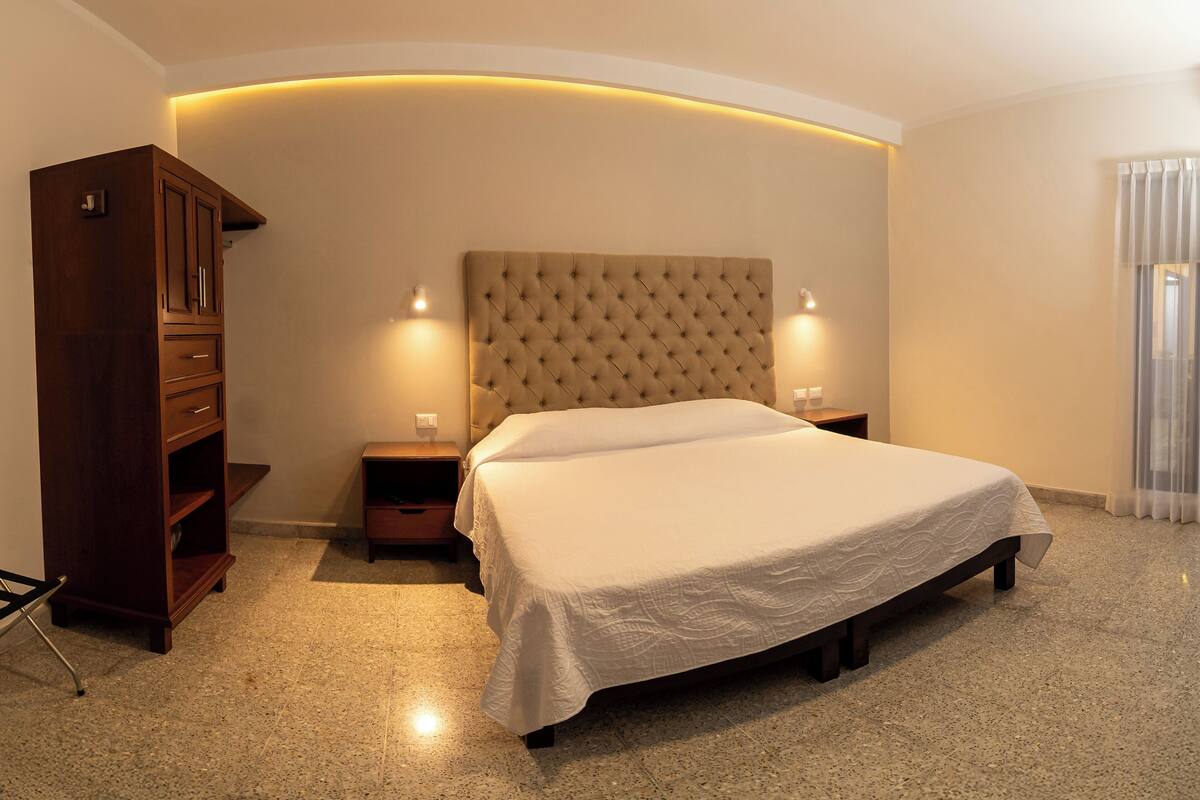 Un dormitorio con una cama grande, un armario, dos mesitas de noche con lámparas y una lámpara de techo curva.