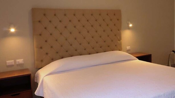 Un lit bien fait, avec une tête de lit capitonnée, dans une chambre d’hôtel.