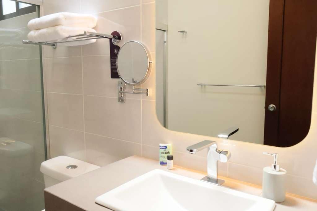 A modern bathroom with a glass shower enclosure, a white sink, a round mirror, and a towel rack.