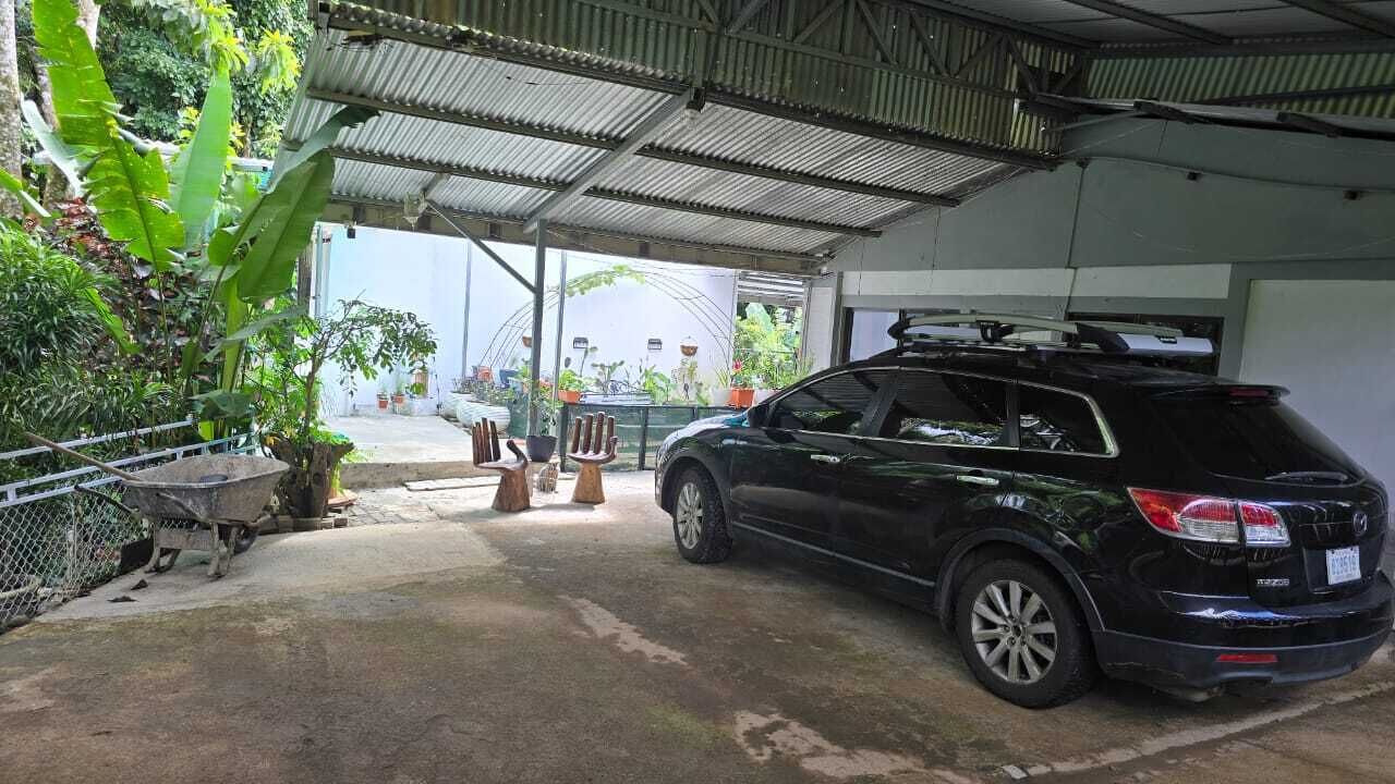 En sort SUV parkeret i en overdækket garage med metal tag, omgivet af plantekasser og en trillebør.