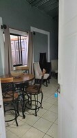 Un comedor con una mesa redonda y sillas, una ventana con cortinas, y una puerta que da a otra habitación.