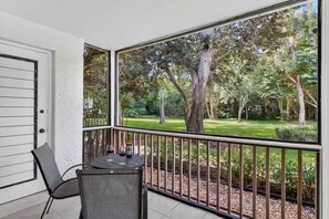 Un balcon avec une table et des chaises, une bouteille de vin et une vue sur un jardin bien entretenu, avec des arbres et de la pelouse.