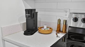 A kitchenette with a Keurig coffee maker, a basket of condiments, and a stove.