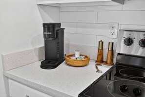 Una kitchenette con una cafetera Keurig, un cesto de condimentos y una estufa.