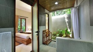 A modern bathroom with a shower, a bathtub, and a toilet. There is a window with curtains and a view of greenery outside. - Mahayoga Ubud Private Pool Villa Spa And Resto (Bali)