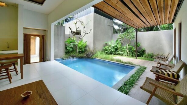 A modern indoor pool area with a concrete wall, wooden ceiling, and seating by the pool. - Mahayoga Ubud Private Pool Villa Spa And Resto (Bali)