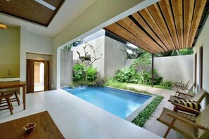 A modern indoor pool area with a concrete wall, wooden ceiling, and seating by the pool. - Mahayoga Ubud Private Pool Villa Spa And Resto (Bali)