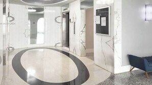 A modern lobby with a curved floor, marble walls, and a blue chair. - private balcony ON THE BEACH with pool 24hr front desk parking spot laundry gym (Hallandale Beach)