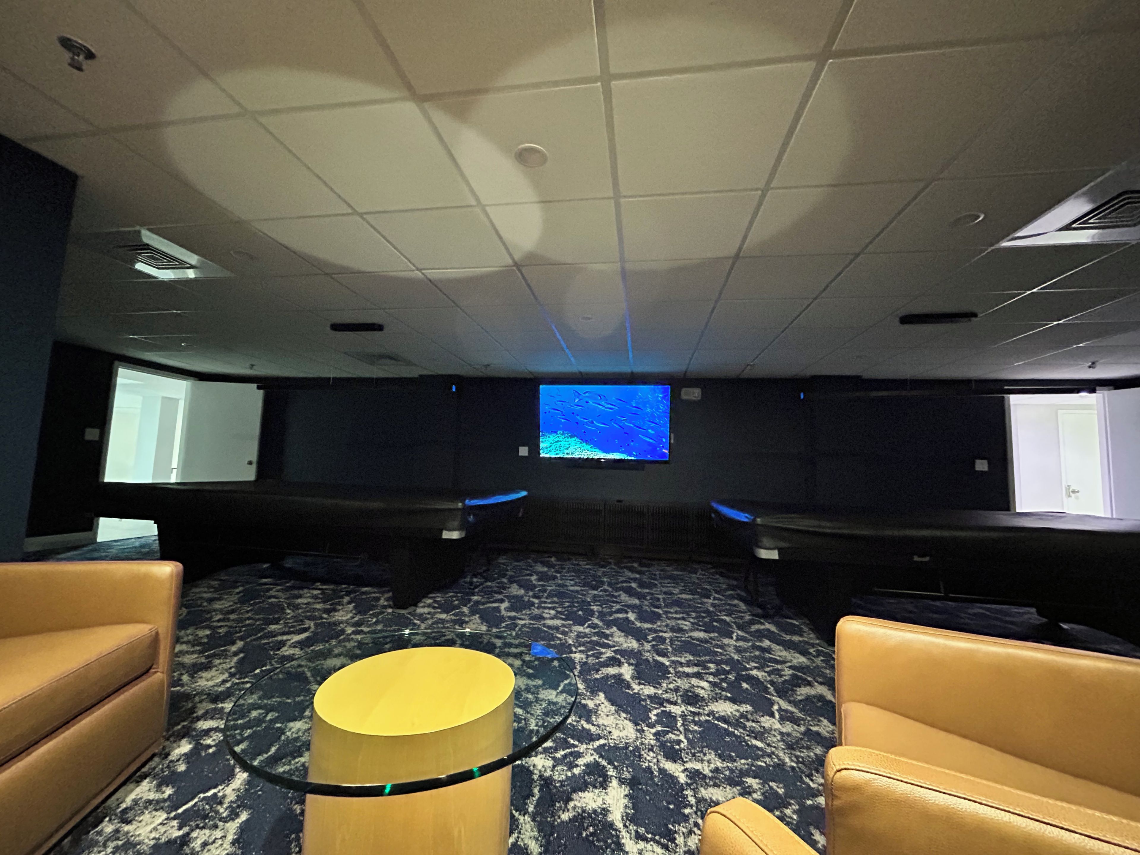 A room with a large screen, two rows of seats, and a central table.