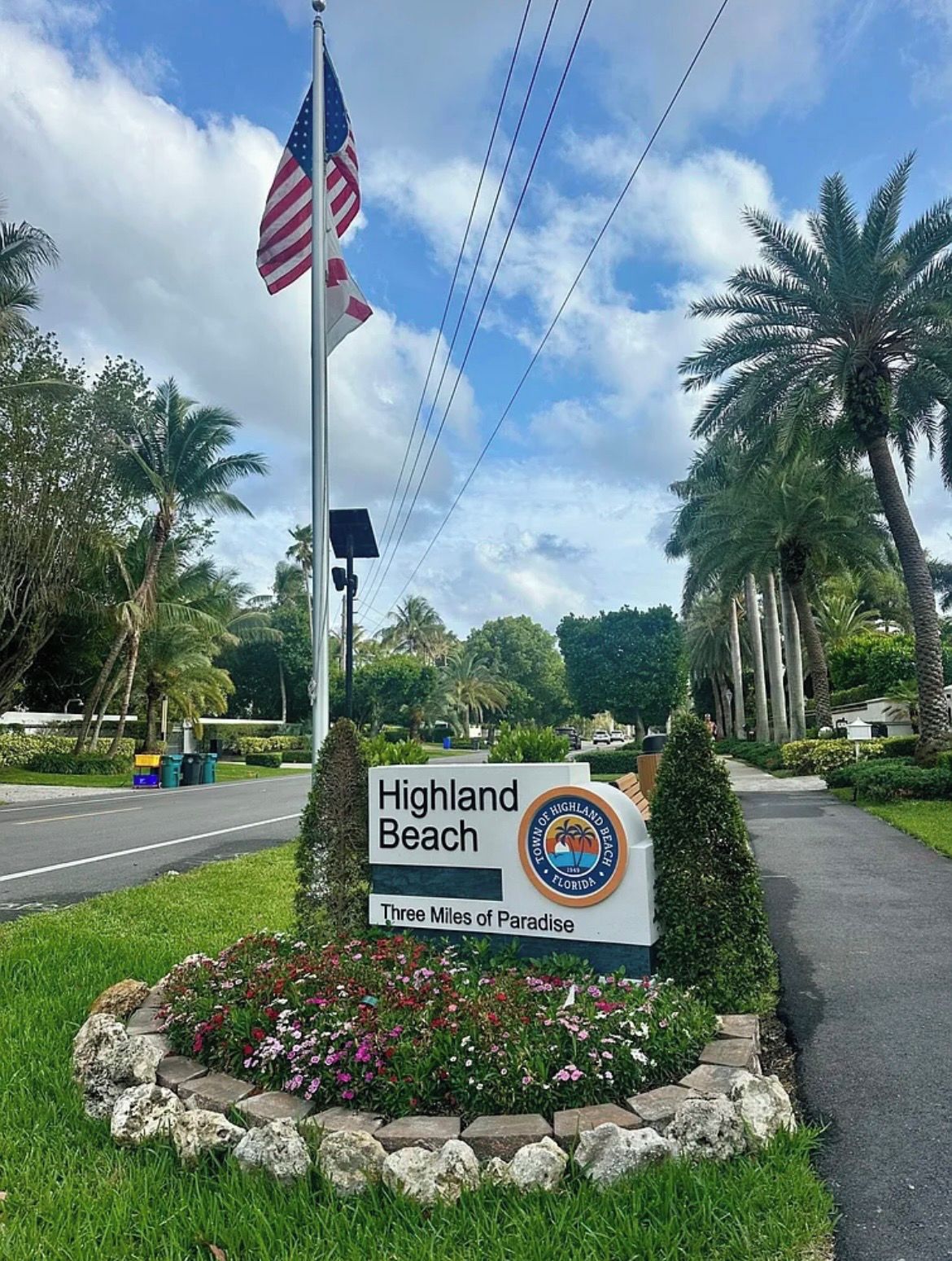 A sign for Highland Beach with a palm tree and flowers.