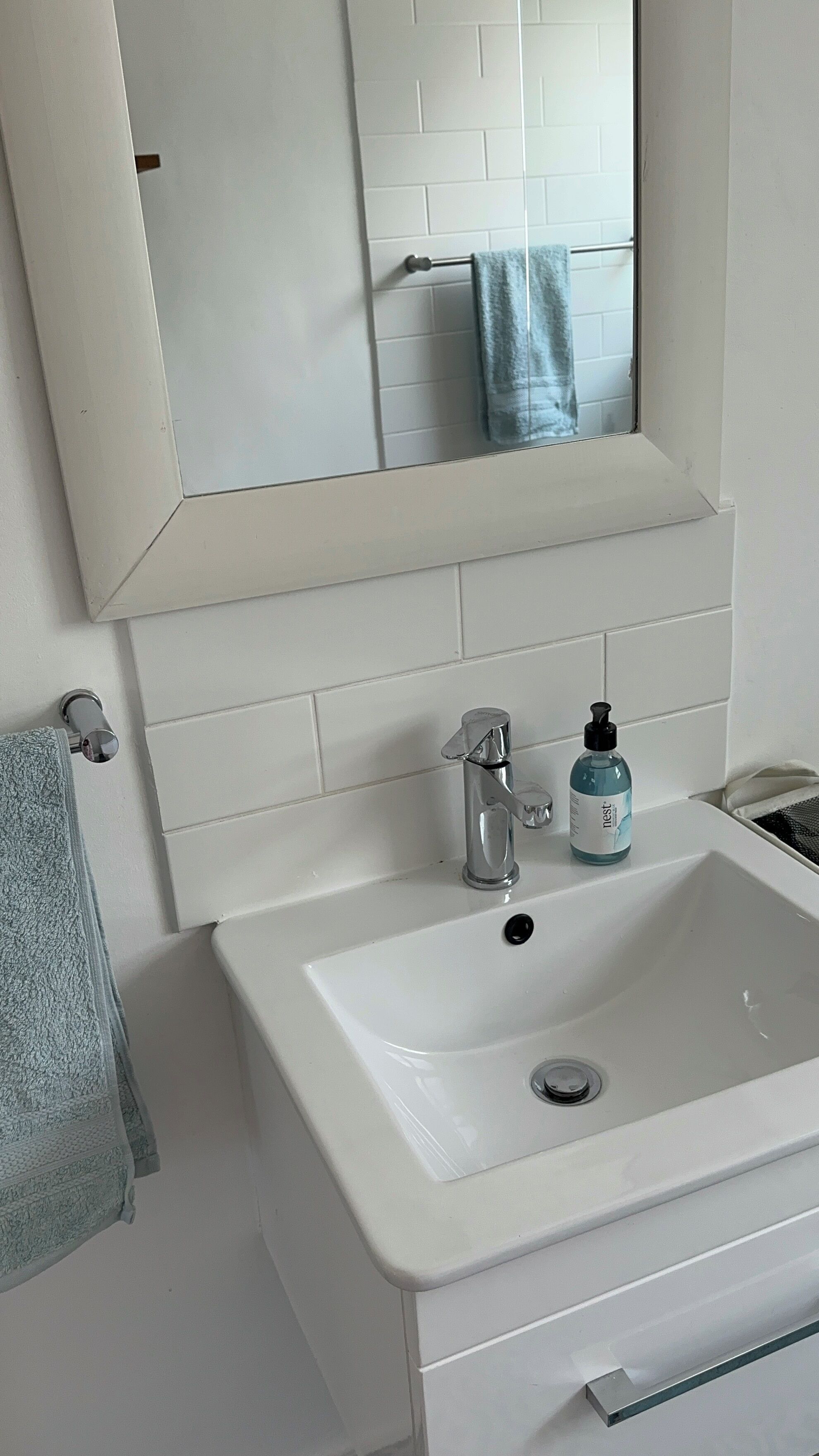 Een badkamer met een witte wasbak, een spiegel en een handdoekhouder.