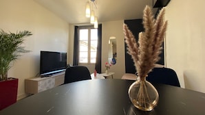A modern living room with a flat-screen TV, a dining table with a vase of pampas grass, and a potted plant. - L'Indigo, charming T2 10 min from the center, Netflix Prime (Poitiers)