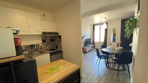 A modern kitchen with white cabinets, a wooden countertop, and a dining area with blue chairs and a round table. - L'Indigo, charming T2 10 min from the center, Netflix Prime (Poitiers)