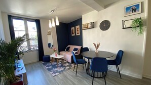 A modern living room with a sofa, a dining table with chairs, a small side table with a vase, a large mirror, and a clock on the wall. - L'Indigo, charming T2 10 min from the center, Netflix Prime (Poitiers)
