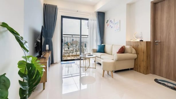 A modern living room with a sofa, a coffee table, and a TV. There is a balcony with a railing and a door leading outside. - SOHO Residence & Hotel (Ho Chi Minh City)