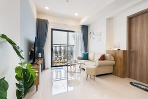 A modern living room with a sofa, a coffee table, and a TV. There is a balcony with a railing and a door leading outside. - SOHO Residence & Hotel (Ho Chi Minh City)