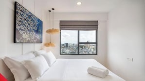 A hotel room with a large bed, a city view, a painting on the wall, and a hanging light fixture. - SOHO Residence & Hotel (Ho Chi Minh City)