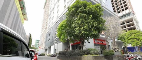 Une vue d’une rue, avec une voiture blanche garée sur le bord, un arbre au milieu et des bâtiments portant des enseignes indiquant « INDE » et « PHILIPPE ».