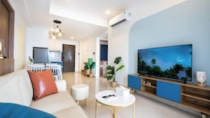 A modern living room with a sofa, a coffee table, a TV, and a dining area in the background. - SOHO Residence & Hotel (Ho Chi Minh City)
