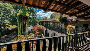 A balcony with a view of a garden, a wooden bridge, and hanging planters. - GARDEN HOTEL (Copan Ruinas)