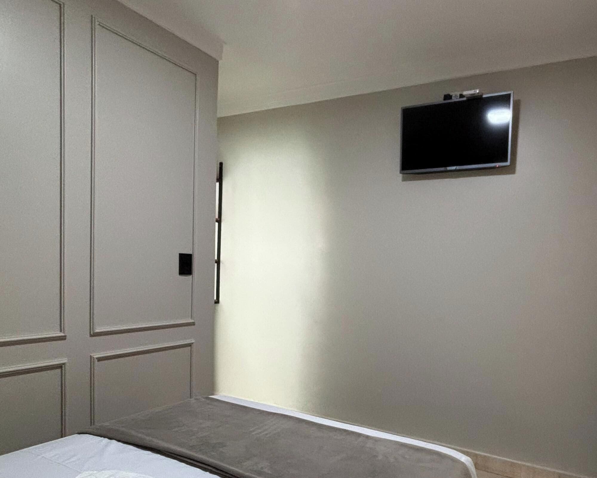 A bedroom with a bed, a wardrobe, and a TV mounted on the wall.