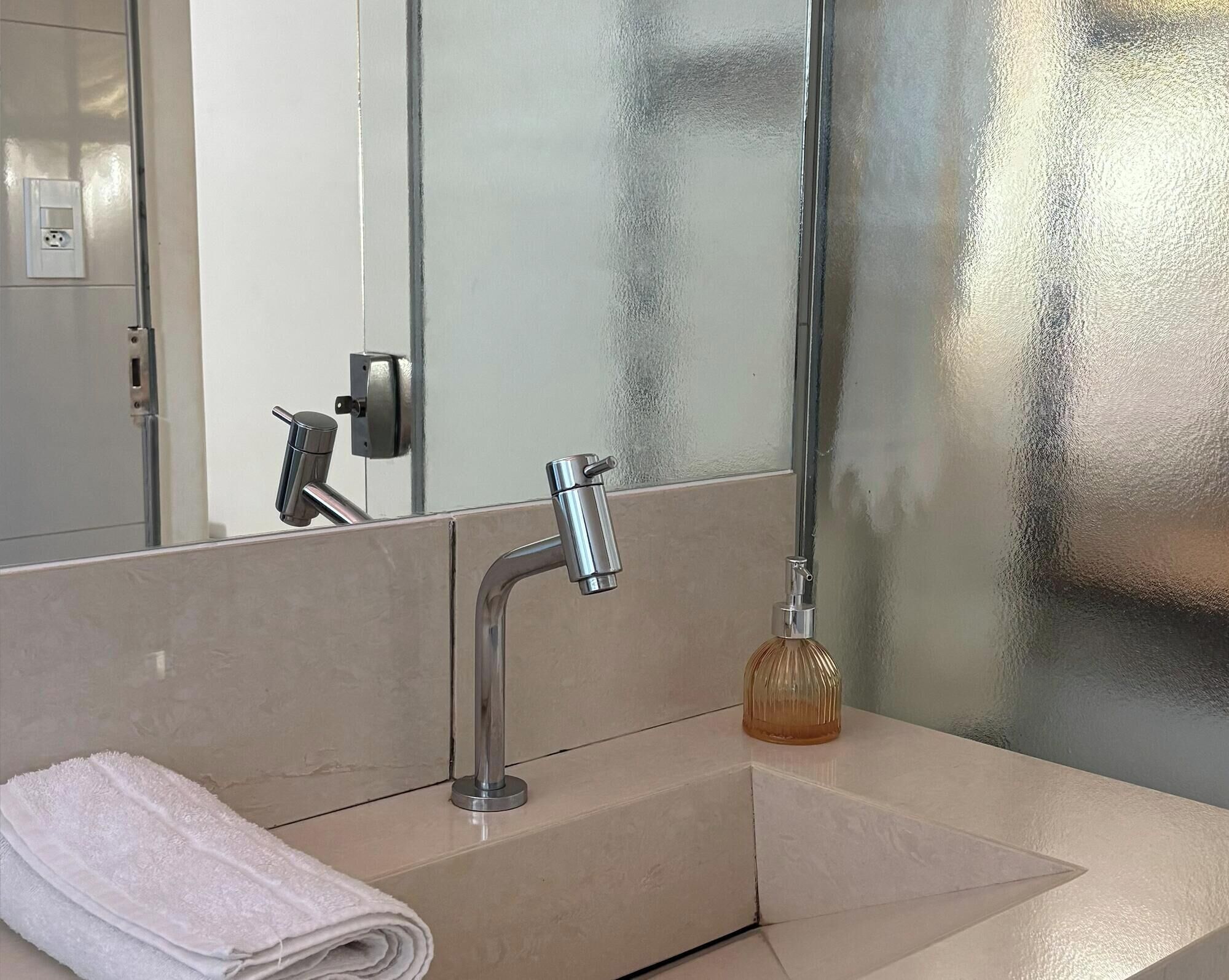 Un baño con lavamanos moderno, espejo y toalla.