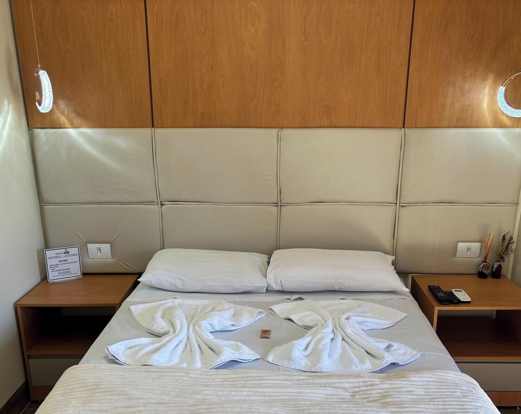 Una habitación de hotel con una cama grande, dos mesitas de noche, un cabecero de madera y un letrero a la izquierda.