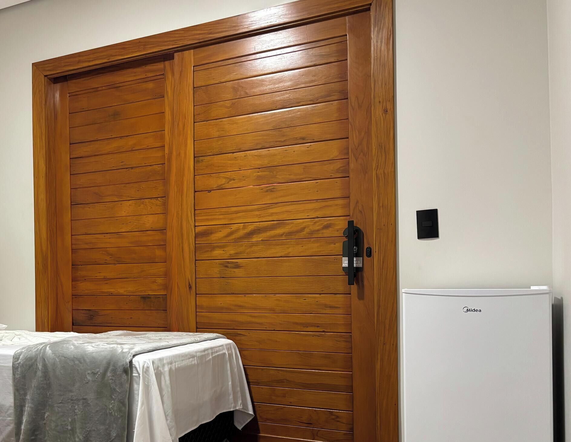 A room with a wooden wardrobe, a white table with a tablecloth, and a white Midea refrigerator.