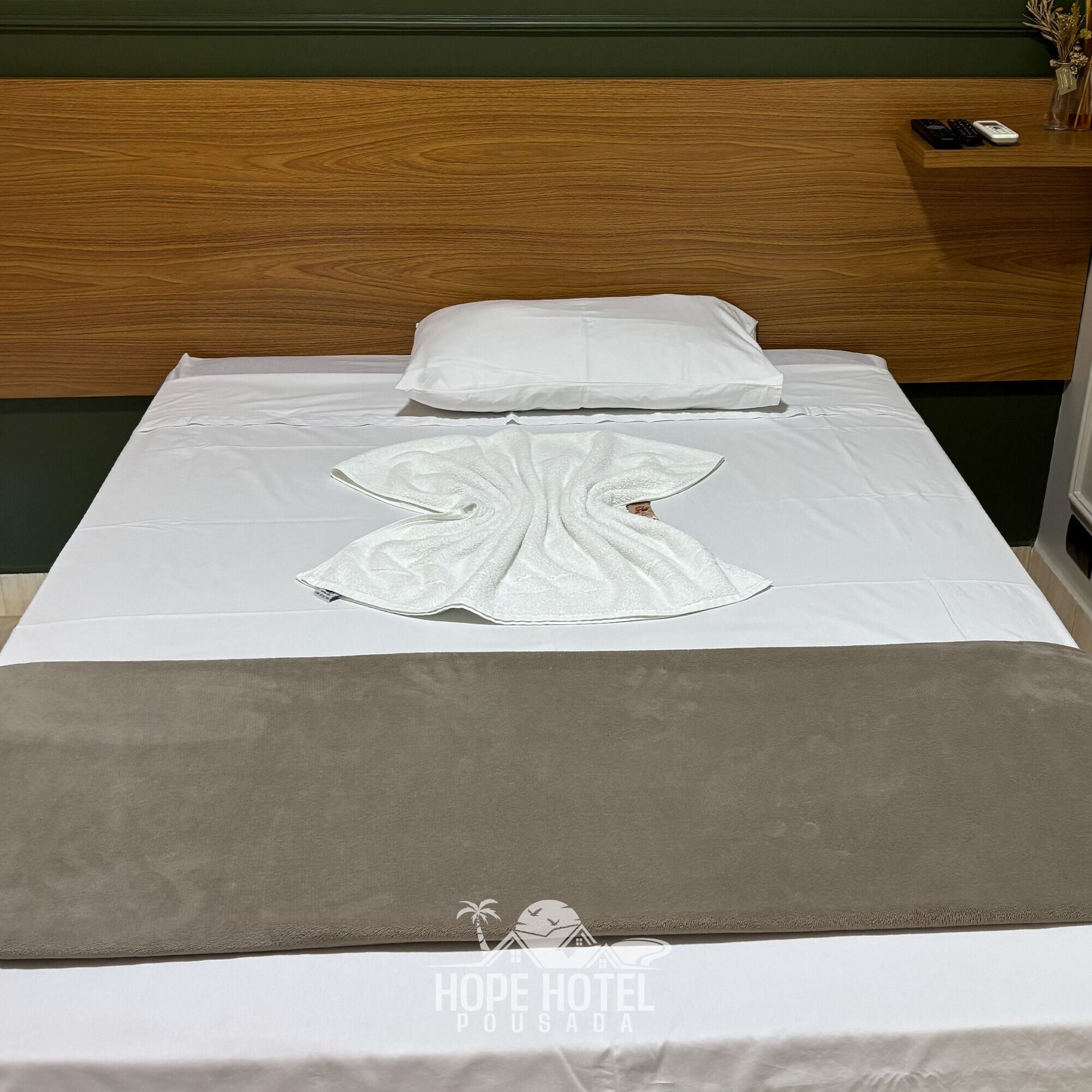 Una cama bien hecha con una almohada blanca, una toalla blanca y una manta gris.