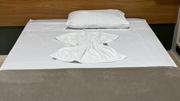 Una cama bien hecha con una almohada blanca, una toalla blanca y una manta gris.