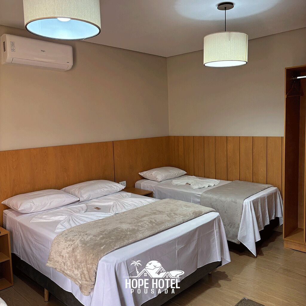 Habitación de hotel con dos camas, cabecero de madera, ventilador de techo, equipo de aire acondicionado e iluminación colgante.