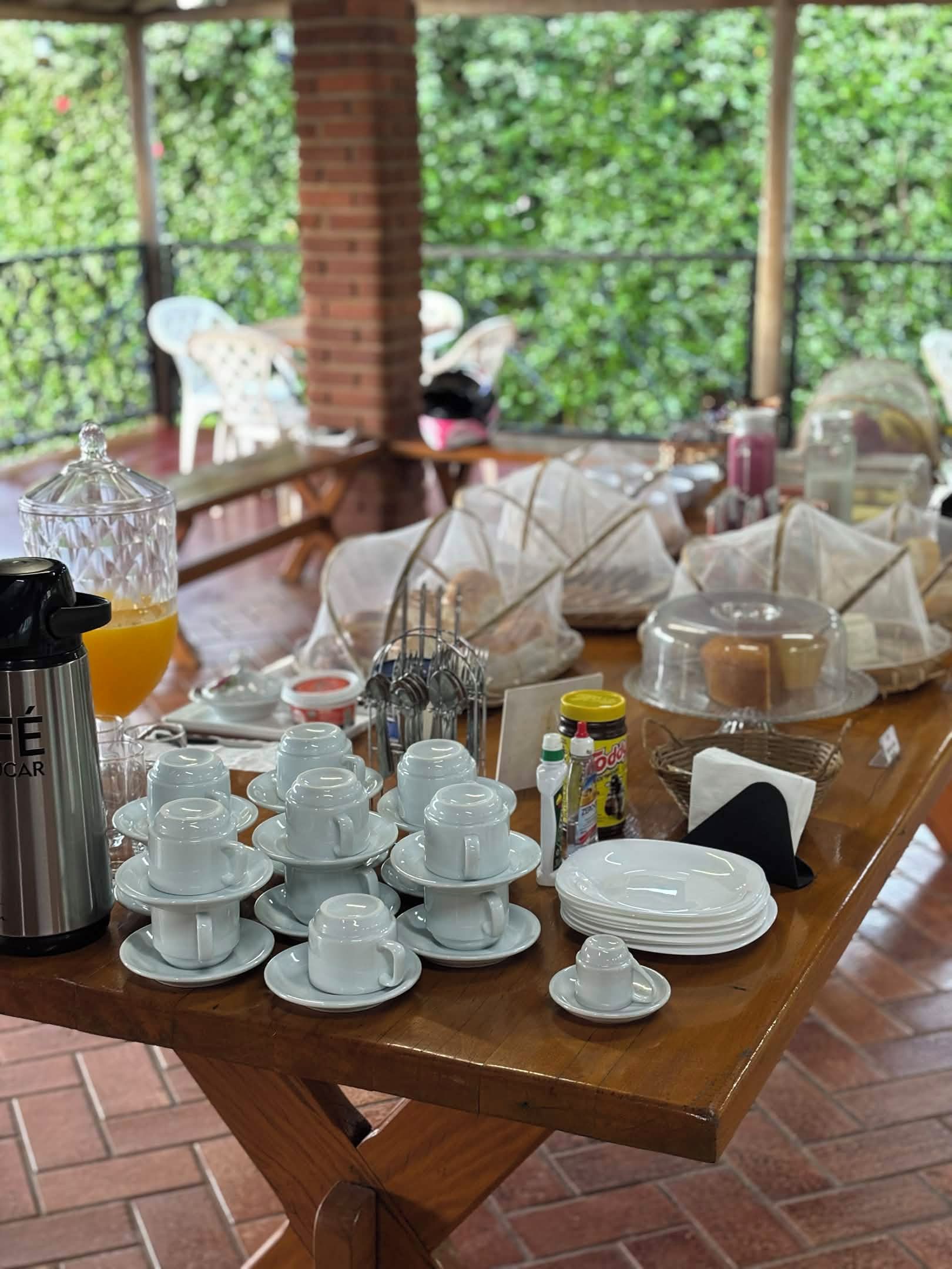 Una mesa de madera con una cafetera, teteras, tazas y platos para el desayuno.