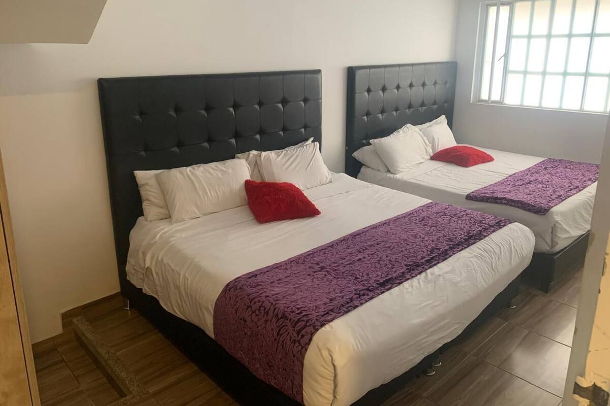 A hotel room with two beds, each with a dark headboard, white bedding, and a purple blanket.
