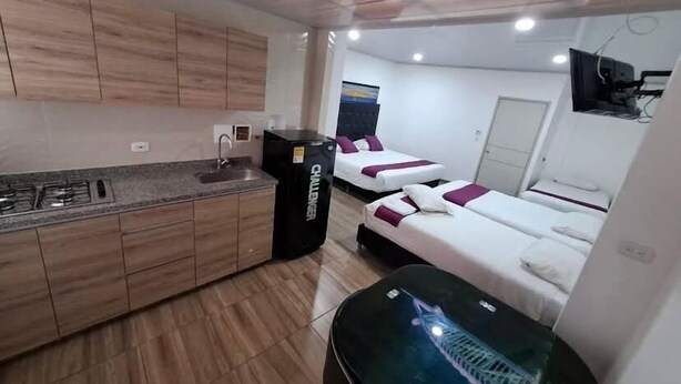 Habitación de hotel compacta con kitchenette, dos camas, televisor y una pequeña mesa.