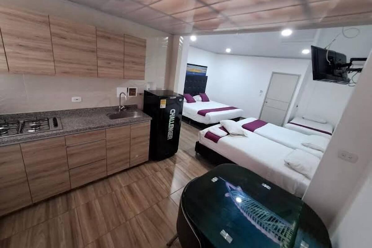 A compact hotel room with a kitchenette, two beds, a TV, and a small table.