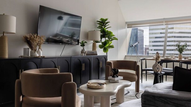 A modern living room with a large flat-screen TV, a dark-colored cabinet, a round coffee table, and a sofa. - Resort Style Property 2B/2B walk to Everything! (Cleveland)