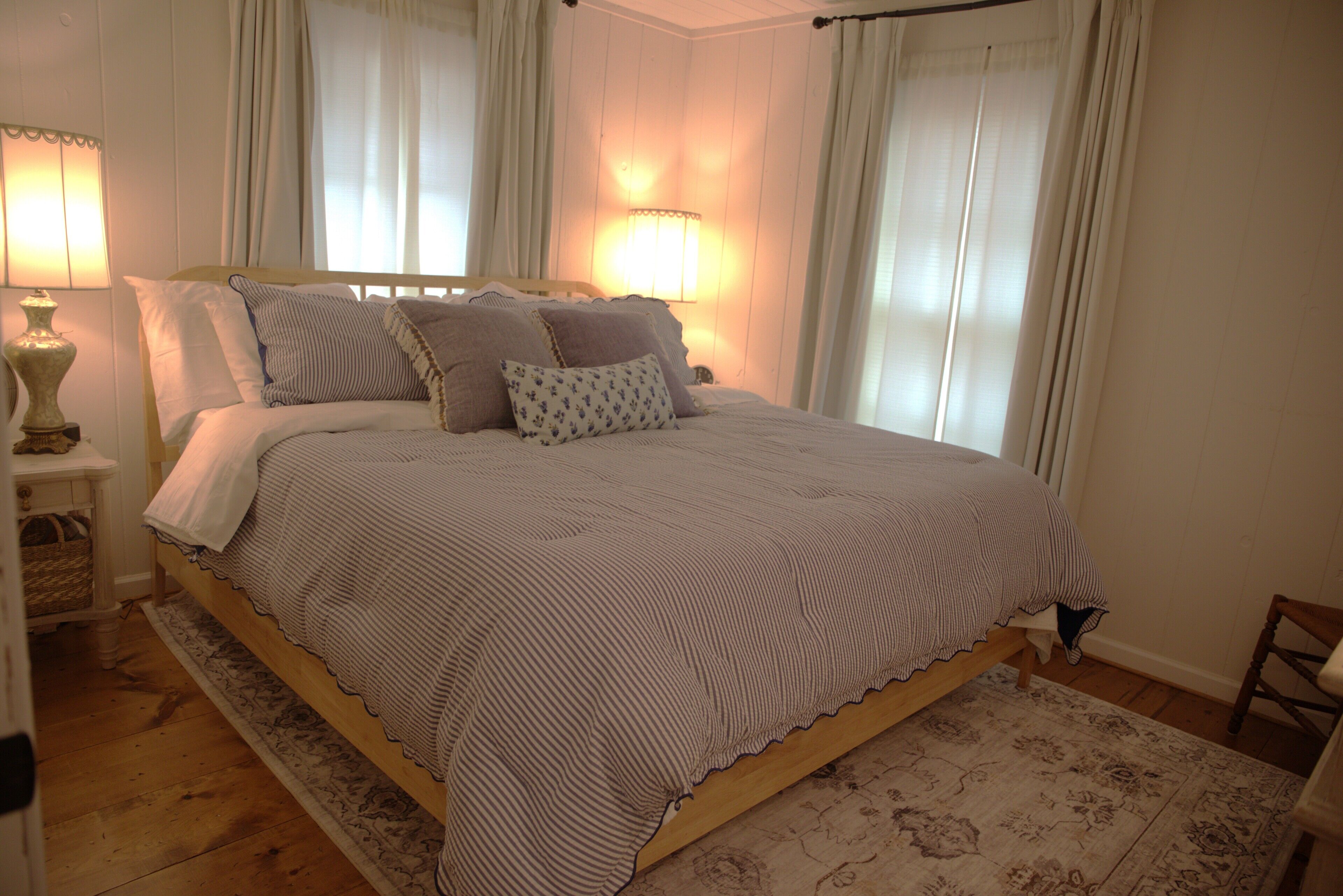 A neatly made bed with a striped bedspread, a bedside lamp, and a floral-patterned rug.