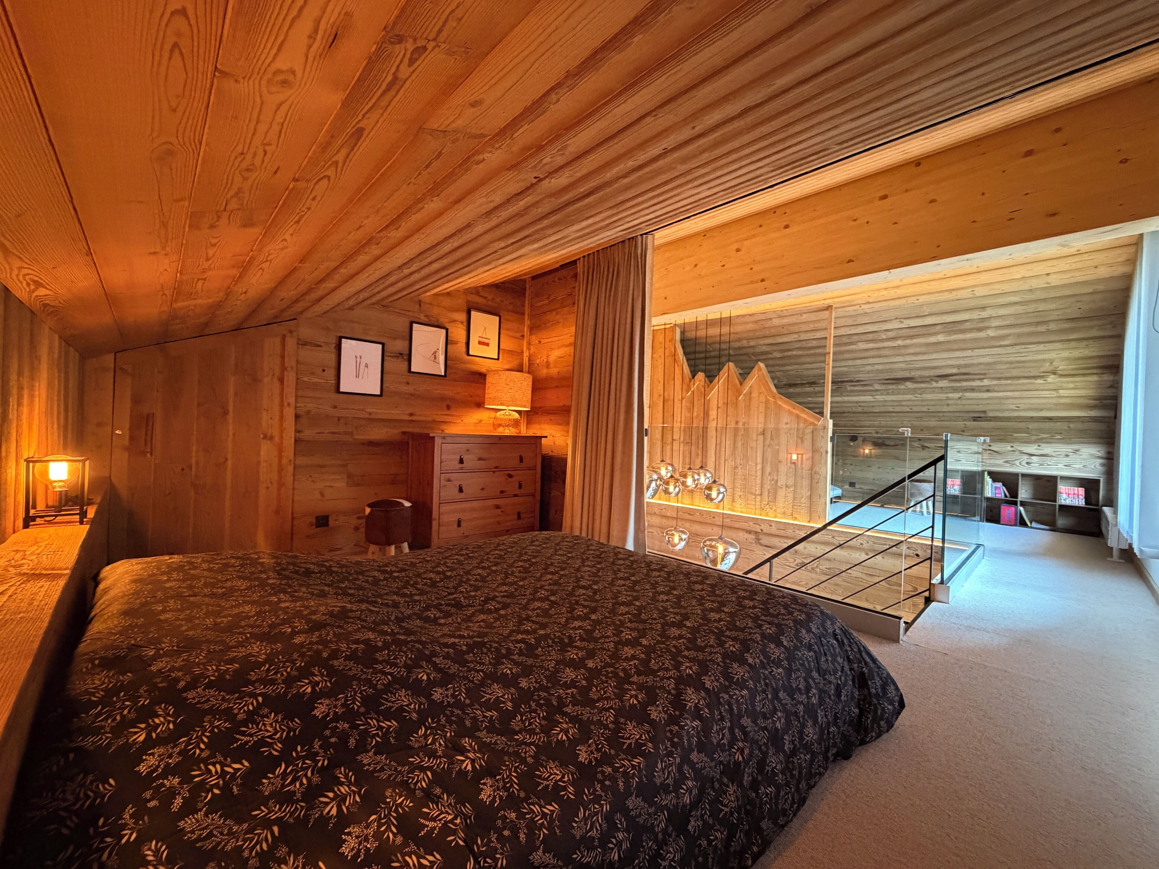 Ein gemütliches Schlafzimmer mit einem großen Bett, Holzwänden, einem Schminktisch und einer Treppe zu einer oberen Ebene.