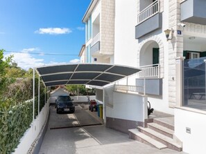 Ein überdachter Parkbereich vor einem zweistöckigen Gebäude mit Balkon.