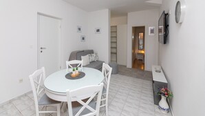 Un soggiorno compatto con zona pranzo, divano, TV a parete e un piccolo corridoio che porta al bagno.