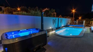 Una vasca idromassaggio e una piscina su un patio con pavimento piastrellato e decorazioni murali a tema palma.