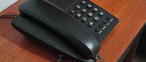 A wooden bedside table with a black telephone and a coiled cord.