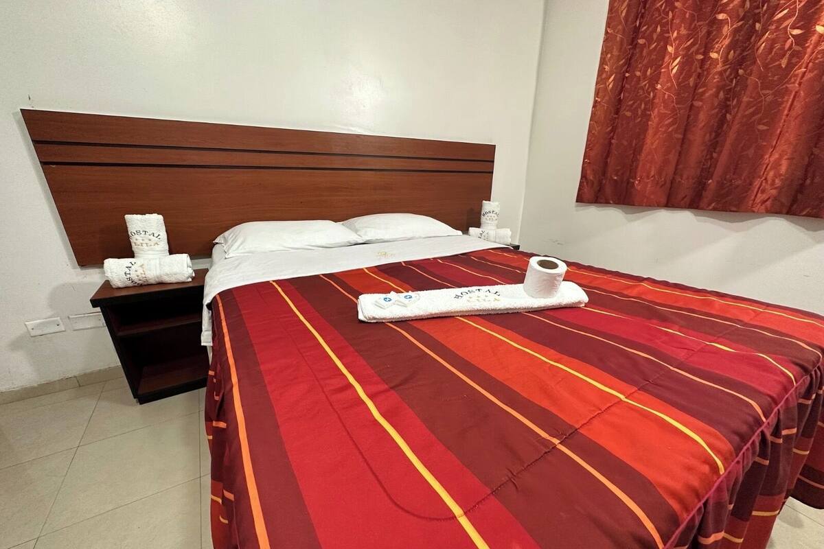 Une chambre d’hôtel avec un lit, une tête de lit en bois, une table de chevet avec des articles de toilette et une couvre-lit à rayures rouges.