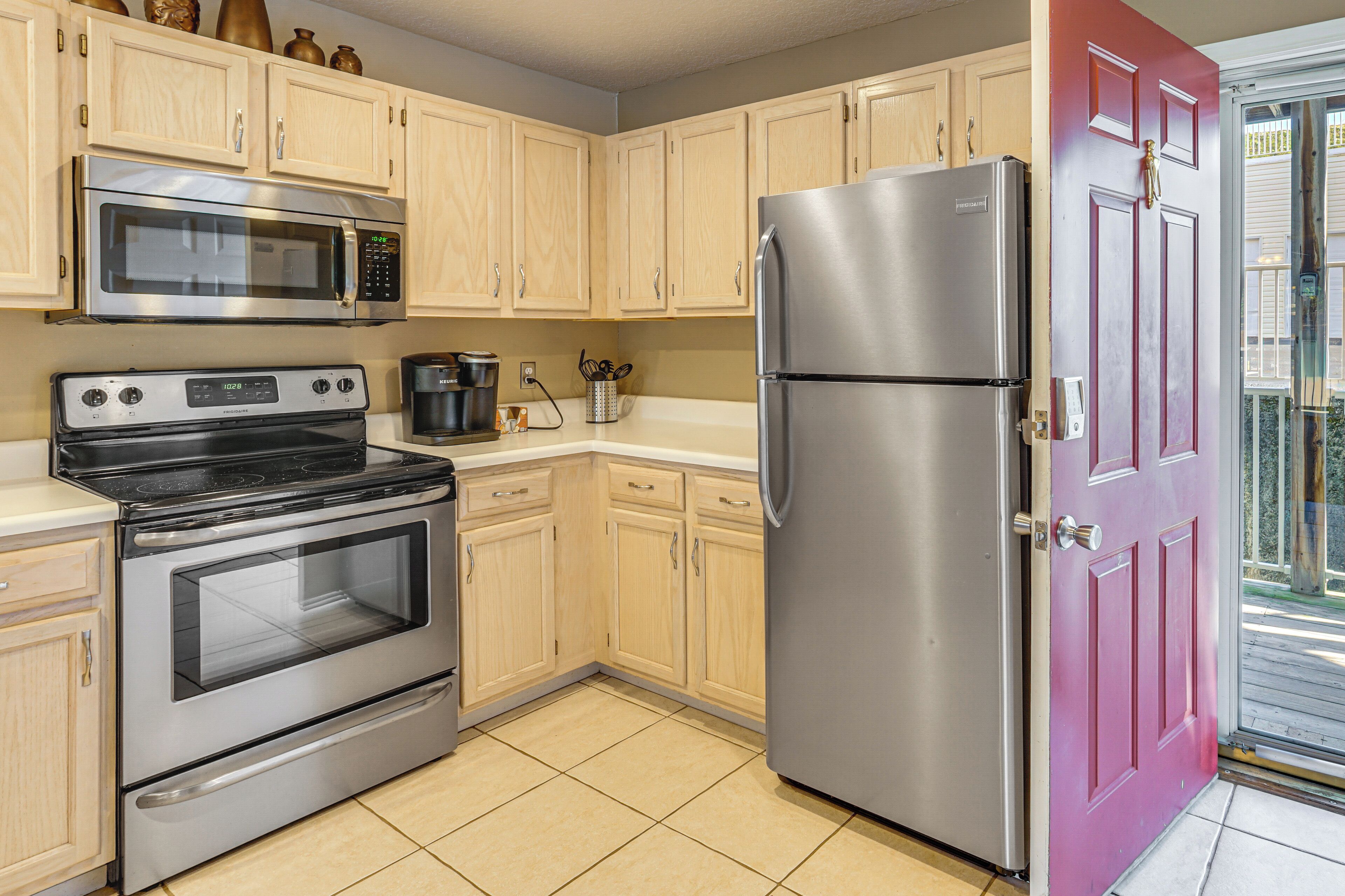 A kitchen with stainless steel appliances, wooden cabinets, and a red door.