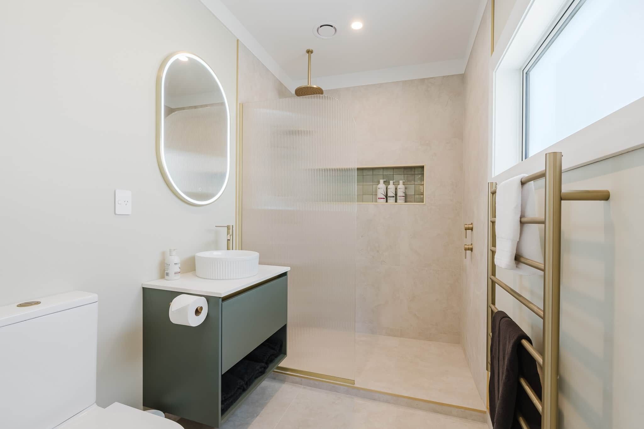 Een moderne badkamer met toilet, wastafel, spiegel, douche en handdoekrek.