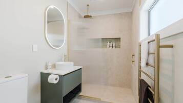 Een moderne badkamer met toilet, wastafel, spiegel, douche en handdoekrek.