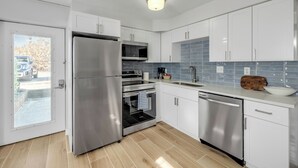 Uma cozinha moderna com eletrodomésticos de aço inoxidável, armários brancos e painel de azulejos.